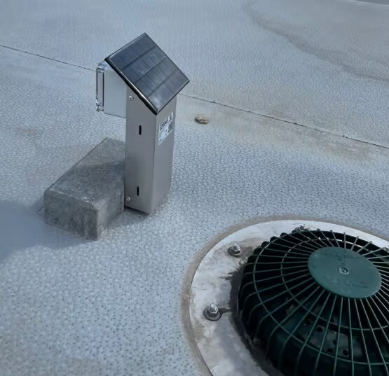 Sense DSW water level sensor with solar cap and ballast block beside a green drain strainer on a flat roof